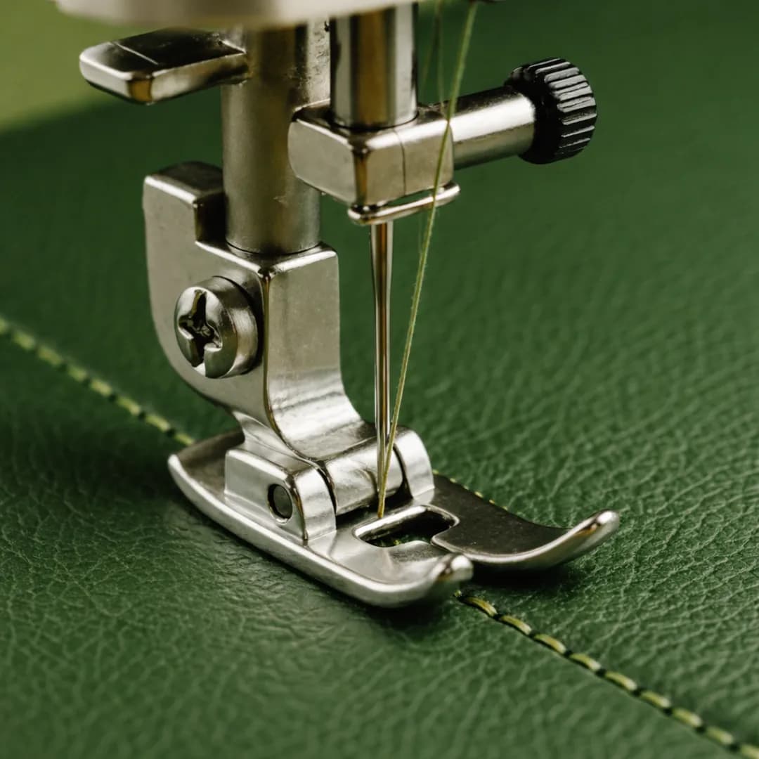 Close-up of an artisan's hands performing traditional saddle stitching on a green leather eyewear case